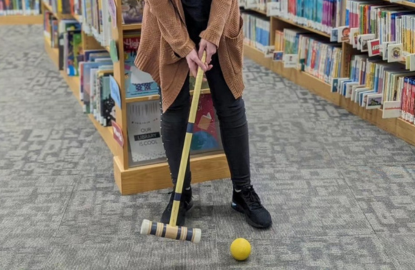A person swings a croquet mallet at a ball